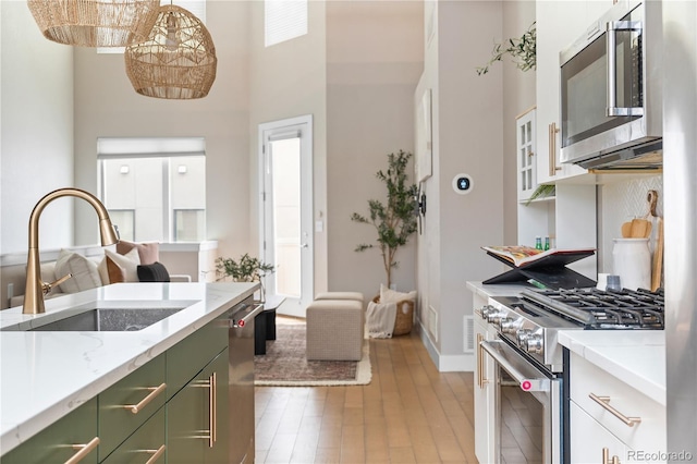 kitchen with sink, light wood-type flooring, pendant lighting, stainless steel appliances, and a high ceiling