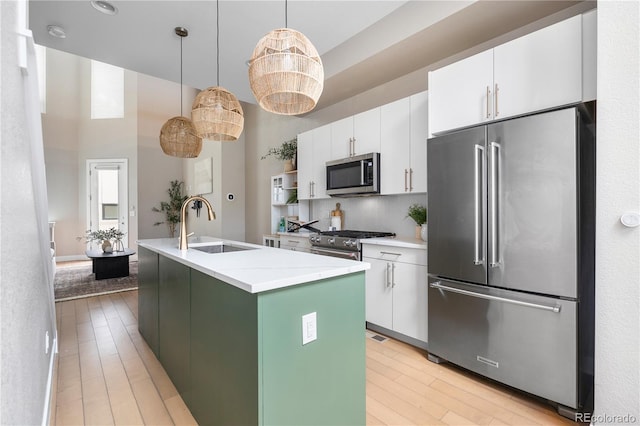 kitchen with sink, a center island with sink, high quality appliances, pendant lighting, and white cabinets