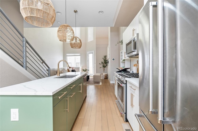 kitchen with pendant lighting, an island with sink, sink, high end appliances, and light wood-type flooring