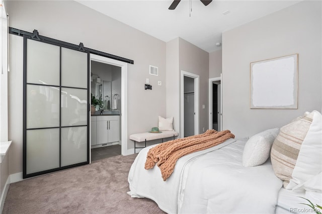 bedroom featuring connected bathroom, a walk in closet, ceiling fan, a barn door, and light carpet