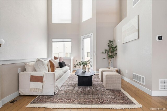 living room featuring a towering ceiling, visible vents, and hardwood / wood-style flooring