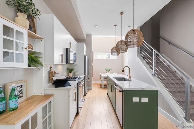kitchen featuring open shelves, white cabinets, a sink, stainless steel appliances, and a center island with sink