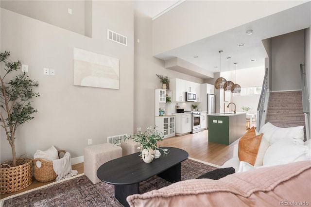 living area featuring stairs, visible vents, light wood-type flooring, and a high ceiling