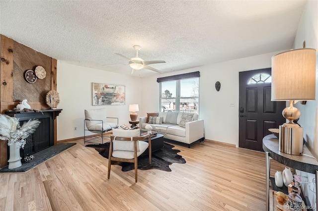 living area featuring a ceiling fan, light wood-style flooring, a fireplace with raised hearth, and a textured ceiling