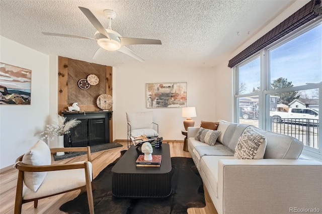 living area featuring a ceiling fan, a textured ceiling, wood finished floors, and a fireplace