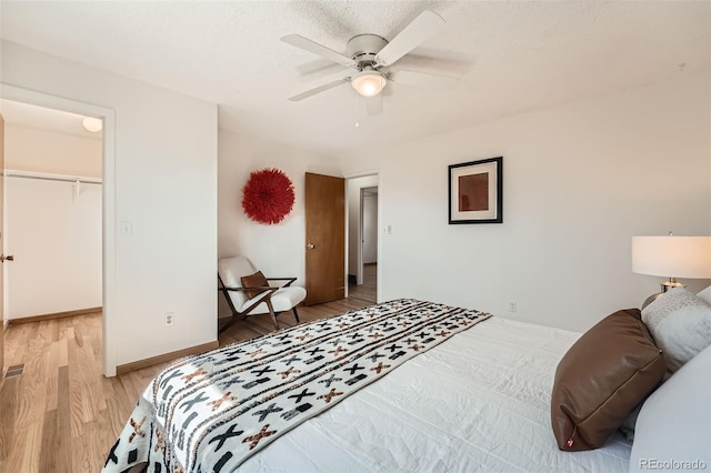 bedroom featuring baseboards, light wood finished floors, ceiling fan, a spacious closet, and a closet