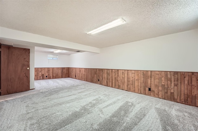 carpeted empty room with wooden walls, a wainscoted wall, and a textured ceiling