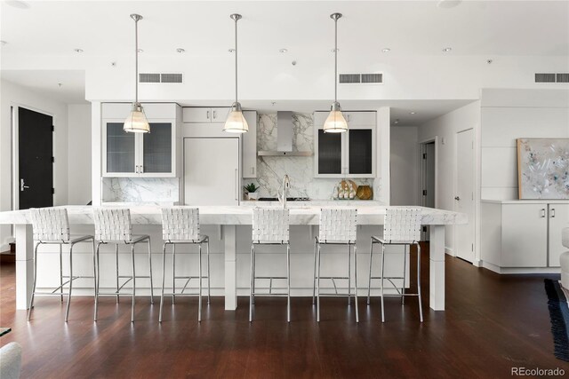 kitchen with decorative backsplash, dark wood-type flooring, a kitchen breakfast bar, and wall chimney range hood