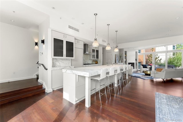 kitchen featuring a breakfast bar area, dark wood-type flooring, visible vents, wall chimney exhaust hood, and tasteful backsplash