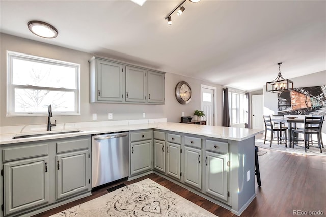 kitchen featuring dark wood-style floors, a peninsula, gray cabinetry, stainless steel dishwasher, and a sink