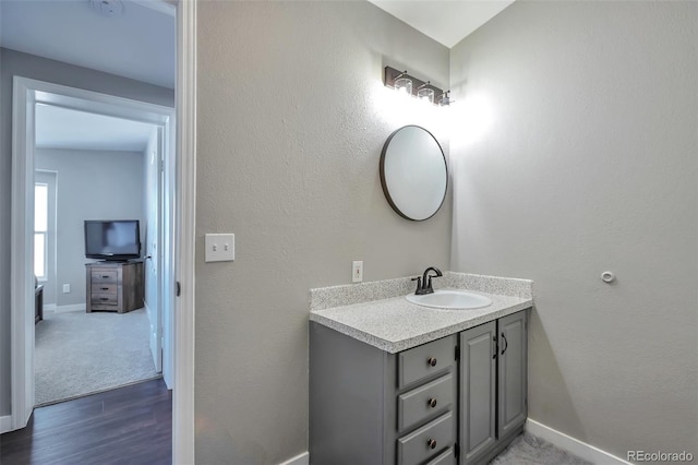 bathroom with a textured wall, baseboards, wood finished floors, and vanity