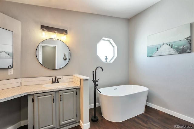 full bath with wood finished floors, a freestanding tub, vanity, and baseboards