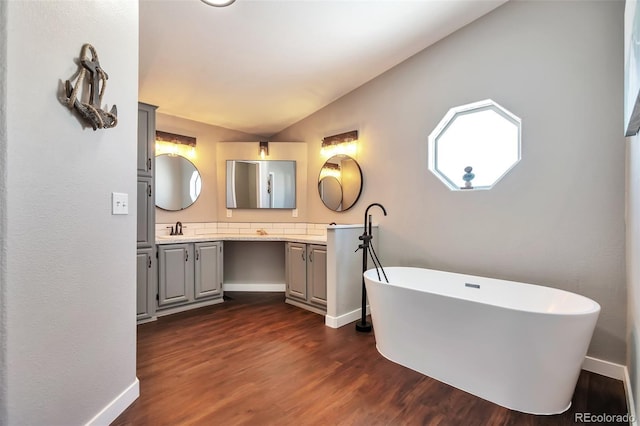 bathroom featuring double vanity, lofted ceiling, a sink, wood finished floors, and a freestanding tub