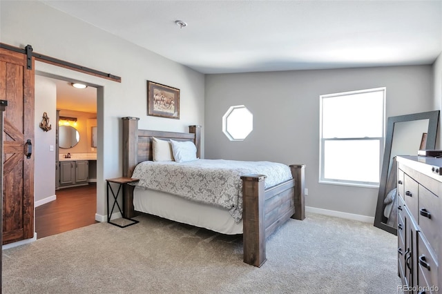 bedroom featuring a barn door, baseboards, ensuite bathroom, and light colored carpet