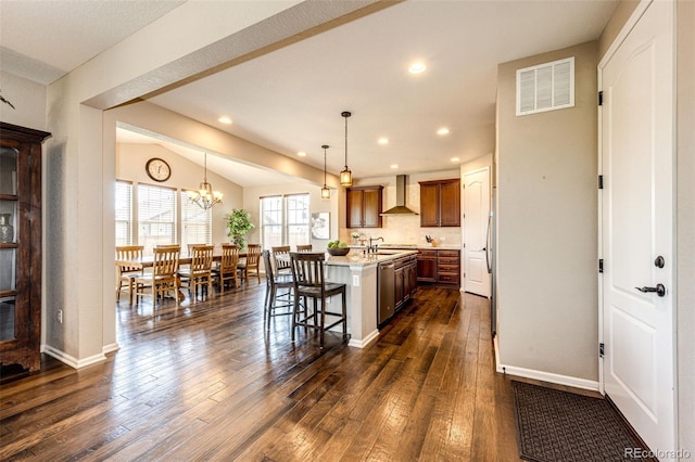 30 S Ider Way, Aurora, CO 80018 - kitchen featuring wall chimney exhaust hood, a center island with sink, dark wood-style floors, a kitchen bar, and decorative light fixtures