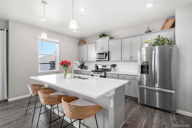 kitchen featuring appliances with stainless steel finishes, decorative light fixtures, a center island with sink, and dark hardwood / wood-style flooring