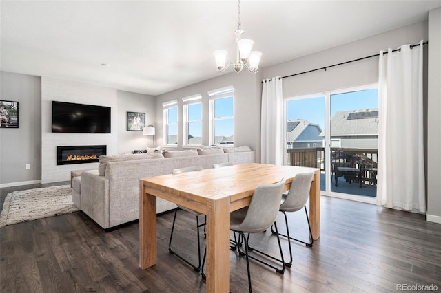 dining room featuring an inviting chandelier, dark hardwood / wood-style floors, a large fireplace, and plenty of natural light