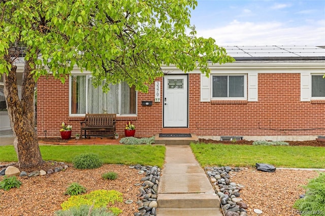 3379 W Wagon Trail Dr, Englewood, CO 80110 - view of exterior entry with brick siding, roof mounted solar panels, and a yard
