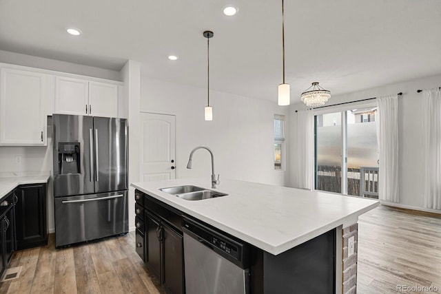 kitchen featuring stainless steel appliances, a sink, white cabinets, light countertops, and an island with sink