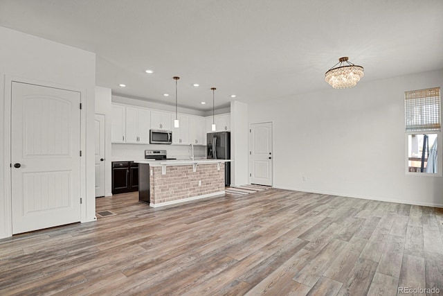 kitchen with a kitchen island with sink, white cabinets, light countertops, appliances with stainless steel finishes, and decorative light fixtures