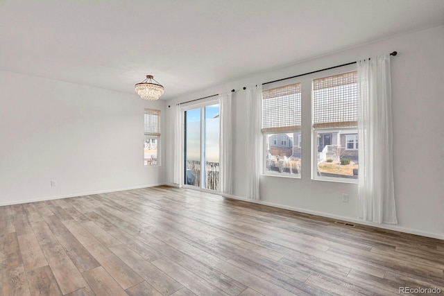 empty room with light wood-style floors, a chandelier, visible vents, and baseboards