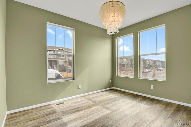 spare room featuring light wood-style floors, baseboards, visible vents, and a chandelier