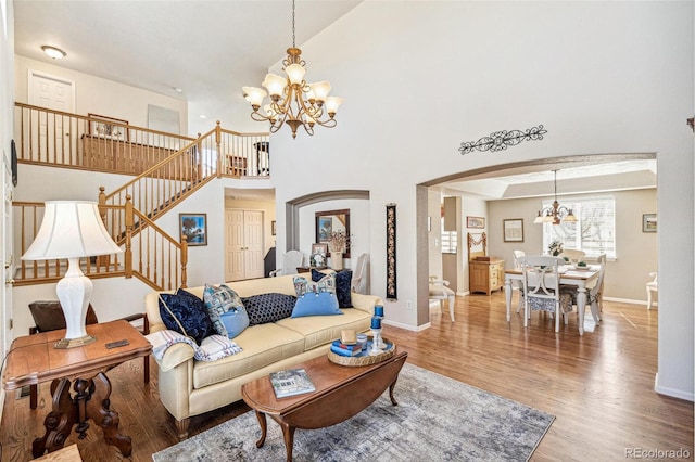 living room with stairway, a high ceiling, an inviting chandelier, wood finished floors, and arched walkways