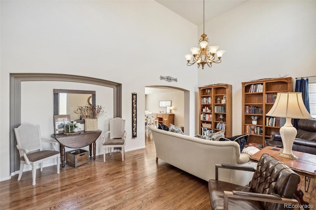 living area featuring wood finished floors, baseboards, high vaulted ceiling, an inviting chandelier, and arched walkways