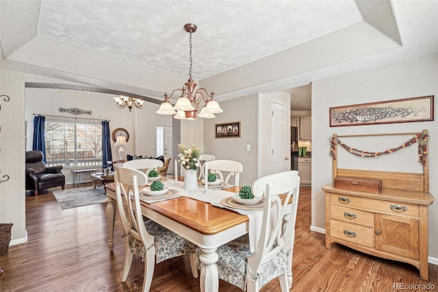 dining area with wood finished floors, baseboards, a textured ceiling, a raised ceiling, and a chandelier