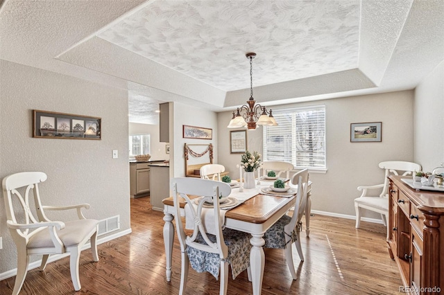 dining area with plenty of natural light, light wood-style flooring, a textured ceiling, and a tray ceiling