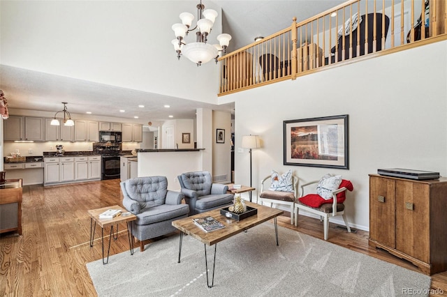 living area with a notable chandelier, recessed lighting, light wood-type flooring, and a towering ceiling