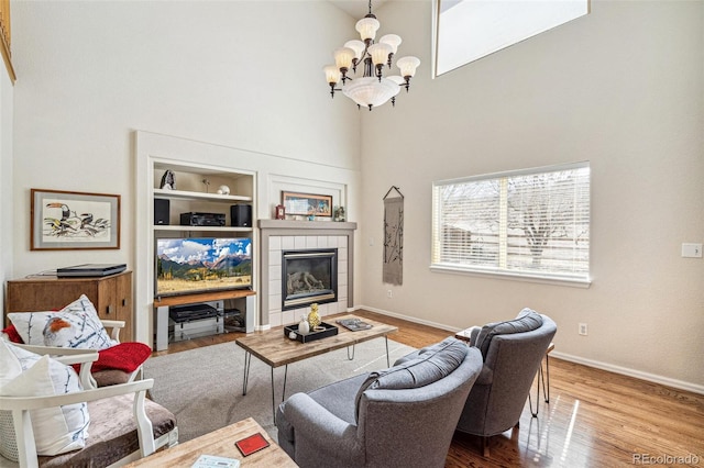 living area featuring built in shelves, a notable chandelier, wood finished floors, baseboards, and a tile fireplace