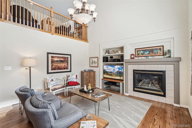 living room featuring a chandelier, a fireplace, a high ceiling, and wood finished floors