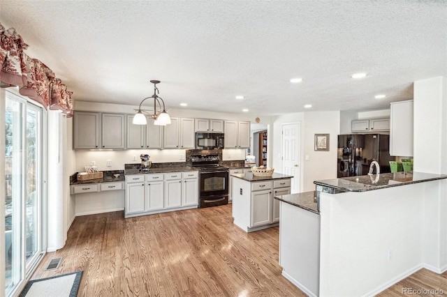 kitchen featuring visible vents, a kitchen island, dark stone counters, light wood-style flooring, and black appliances