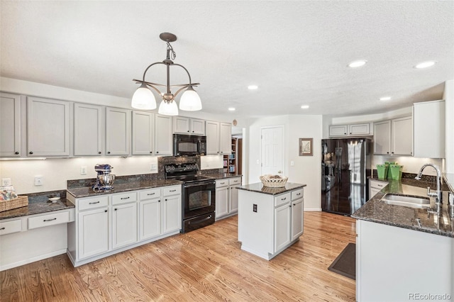 kitchen with a kitchen island, dark stone counters, light wood-style flooring, a sink, and black appliances