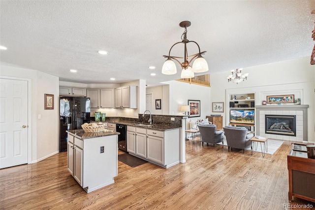 kitchen featuring black appliances, a sink, open floor plan, a fireplace, and light wood finished floors