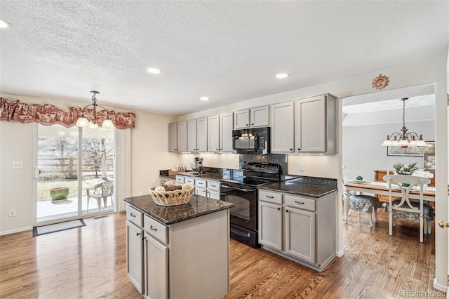 kitchen with dark stone countertops, light wood-style floors, black appliances, and an inviting chandelier