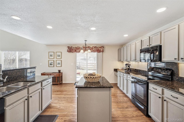 kitchen with light wood finished floors, a center island, dark stone countertops, black appliances, and a sink