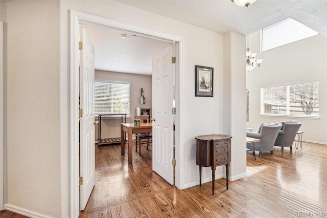 hall featuring an inviting chandelier, light wood-style flooring, a textured ceiling, and baseboards