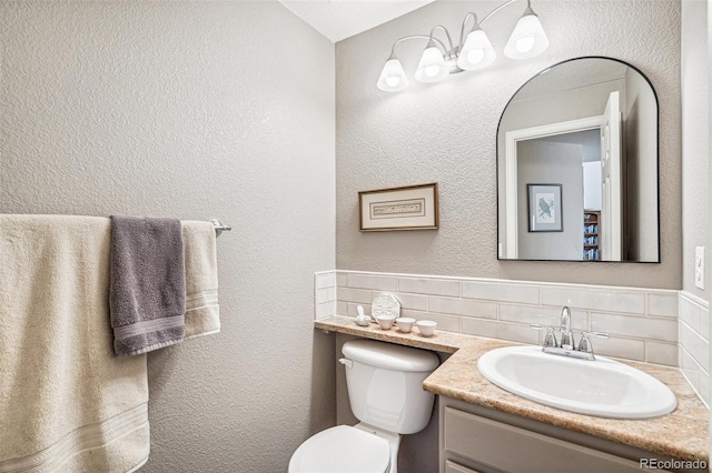 bathroom with toilet, vanity, and a textured wall