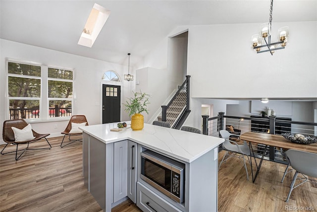 kitchen with decorative light fixtures, light hardwood / wood-style flooring, stainless steel microwave, gray cabinets, and vaulted ceiling with skylight