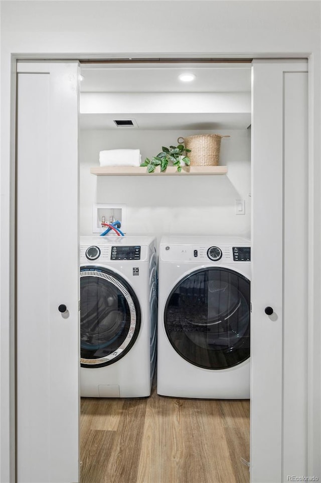 clothes washing area featuring separate washer and dryer and light hardwood / wood-style floors