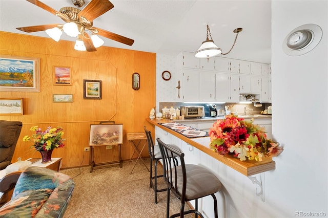 kitchen with light colored carpet, a kitchen breakfast bar, white cabinets, and ceiling fan