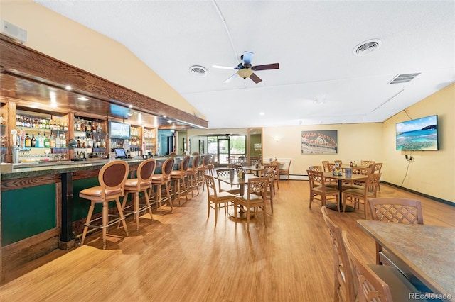 dining space with indoor bar, lofted ceiling, ceiling fan, and light hardwood / wood-style flooring