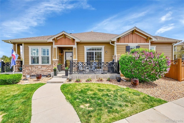 craftsman house featuring board and batten siding, fence, stone siding, and a front yard