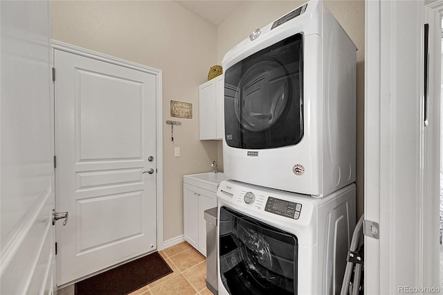 laundry room with cabinet space, baseboards, stacked washing maching and dryer, and light tile patterned floors