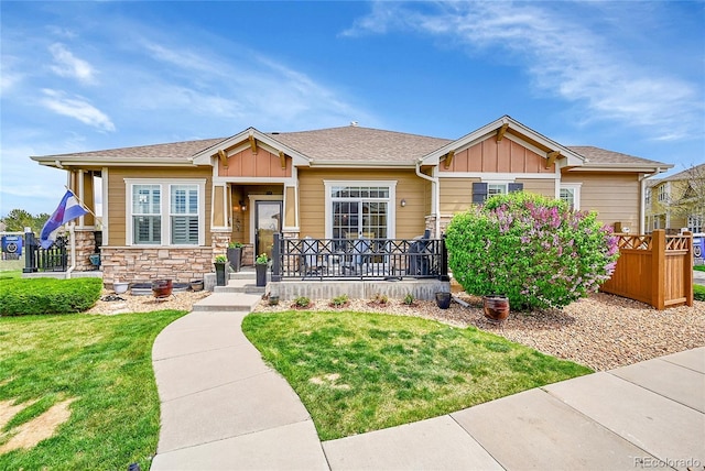 craftsman house with board and batten siding, a front yard, covered porch, and stone siding