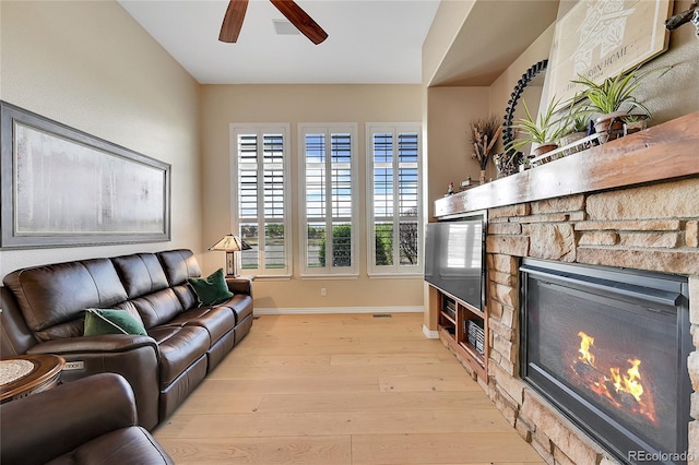 living room with a ceiling fan, visible vents, a fireplace, baseboards, and light wood finished floors