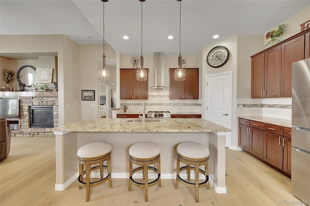 kitchen featuring wall chimney range hood, backsplash, a sink, and light wood finished floors