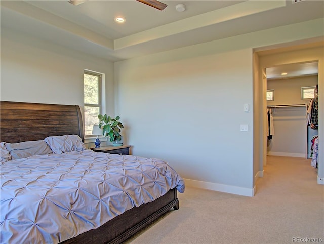 carpeted bedroom with ceiling fan, a tray ceiling, and a spacious closet